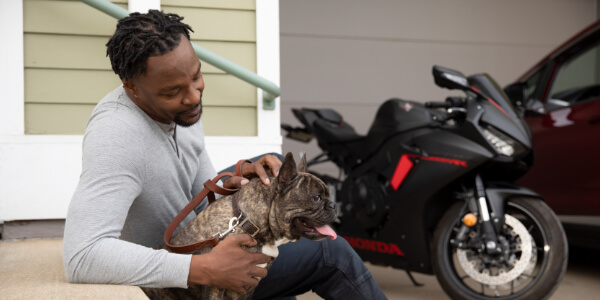 Man relaxing with dog in front of motorcycle and car